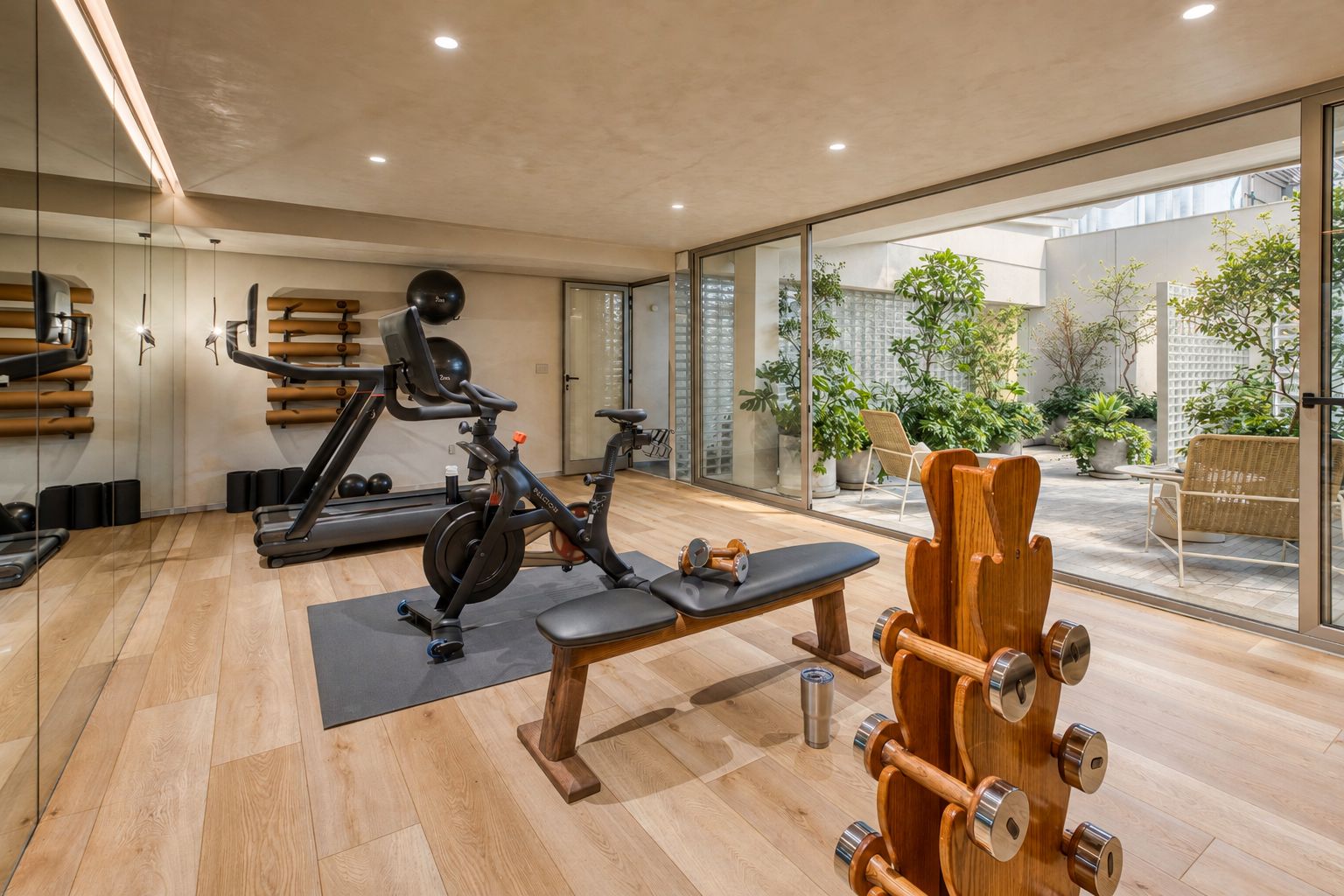 Een moderne sportschool met trainingsapparatuur, een bankje en een uitzicht op het buitenlands terrein door grote ramen.