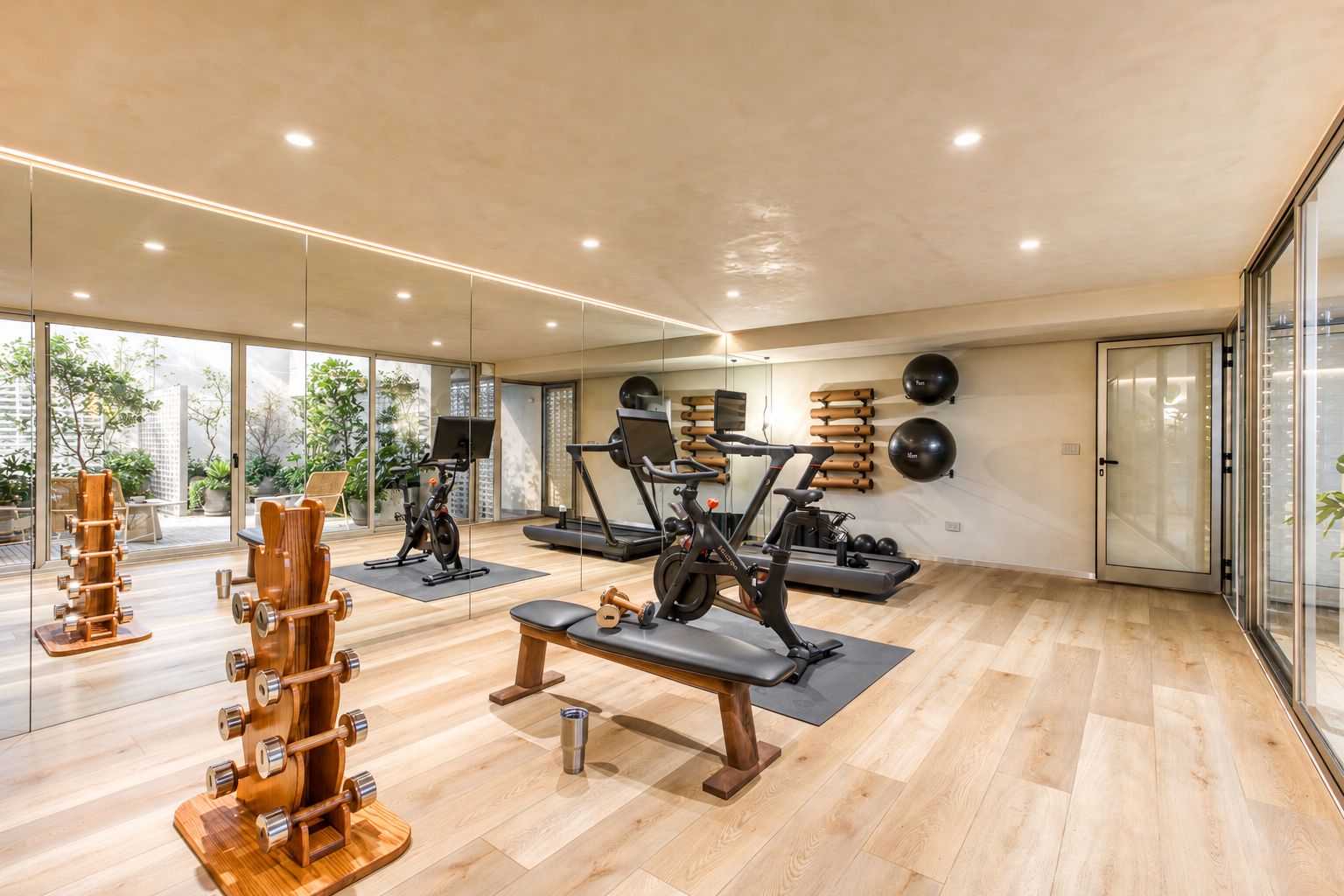 Un gimnasio amplio con equipo de ejercicio, ventanas grandes y suelo de madera.