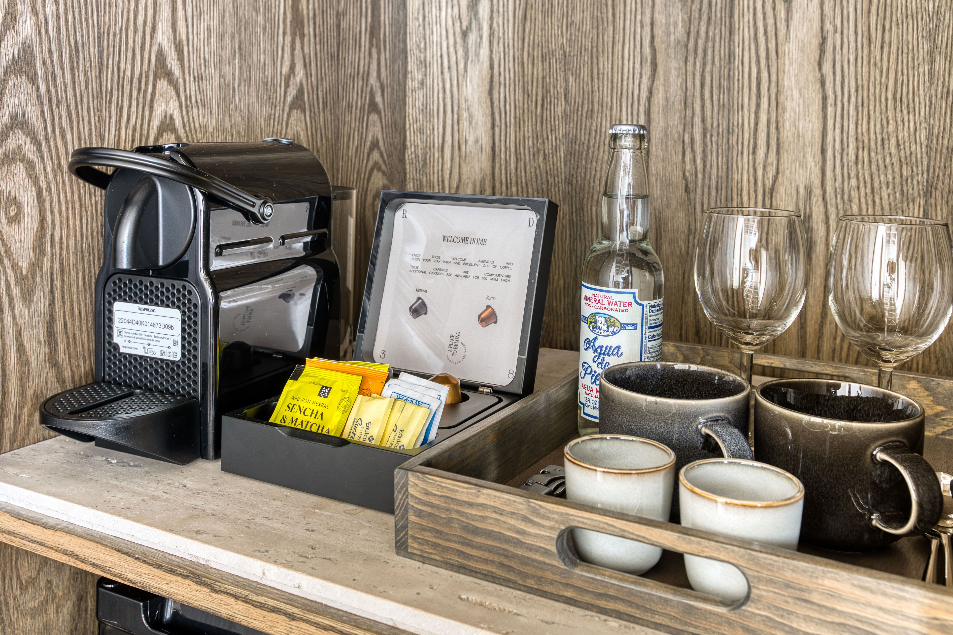 A coffee maker, a bottle of water, and two glasses on a wooden counter.