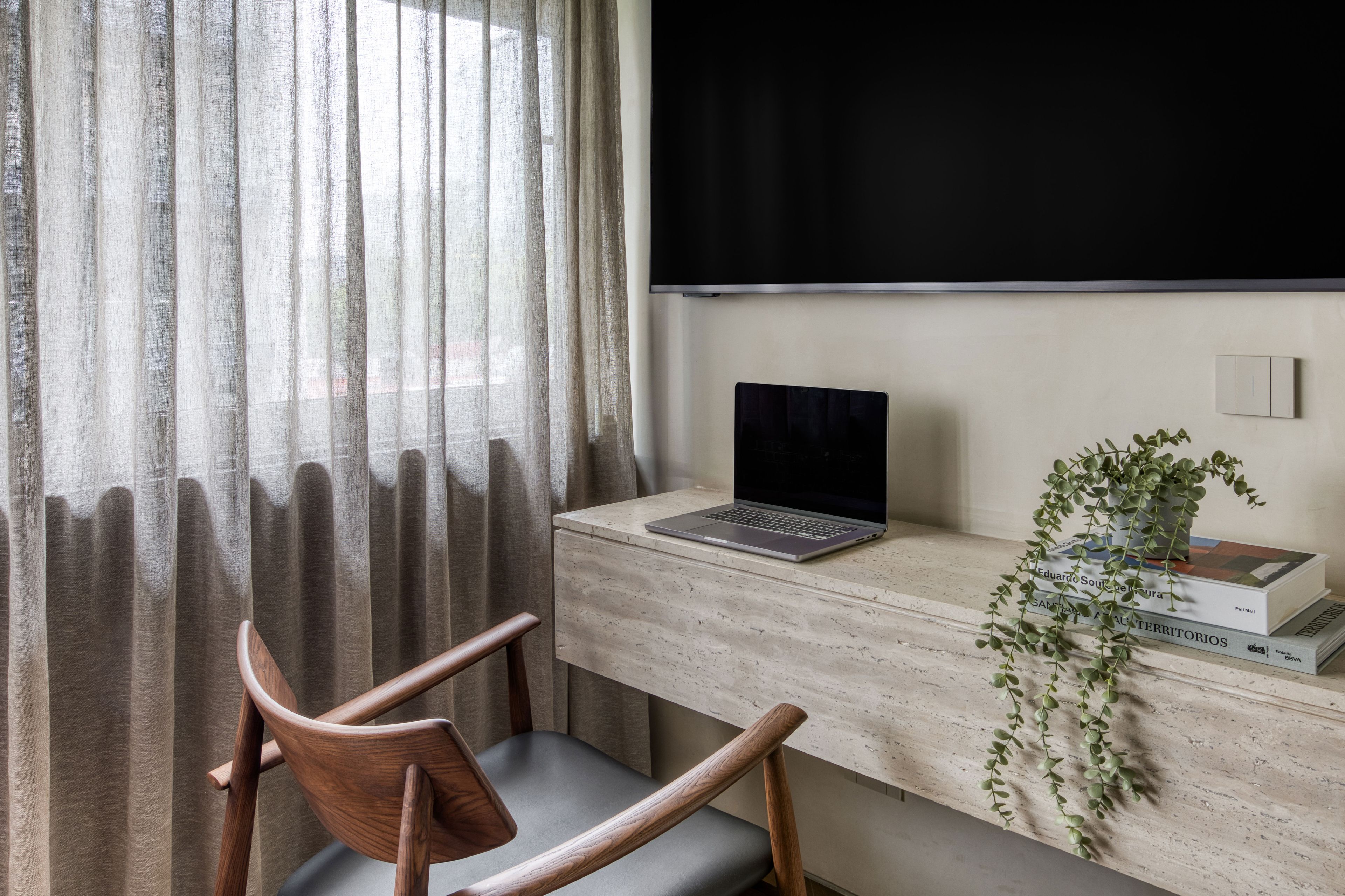 A workspace with a laptop on a wooden desk, a chair, a plant, and a window with curtains.