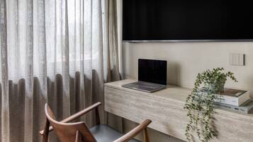 A workspace with a laptop on a wooden desk, a chair, a plant, and a window with curtains.