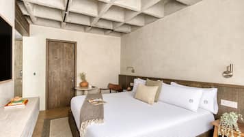 A bedroom with a large bed, a wooden headboard, a bedside table with a lamp, and a small table with a vase and books.