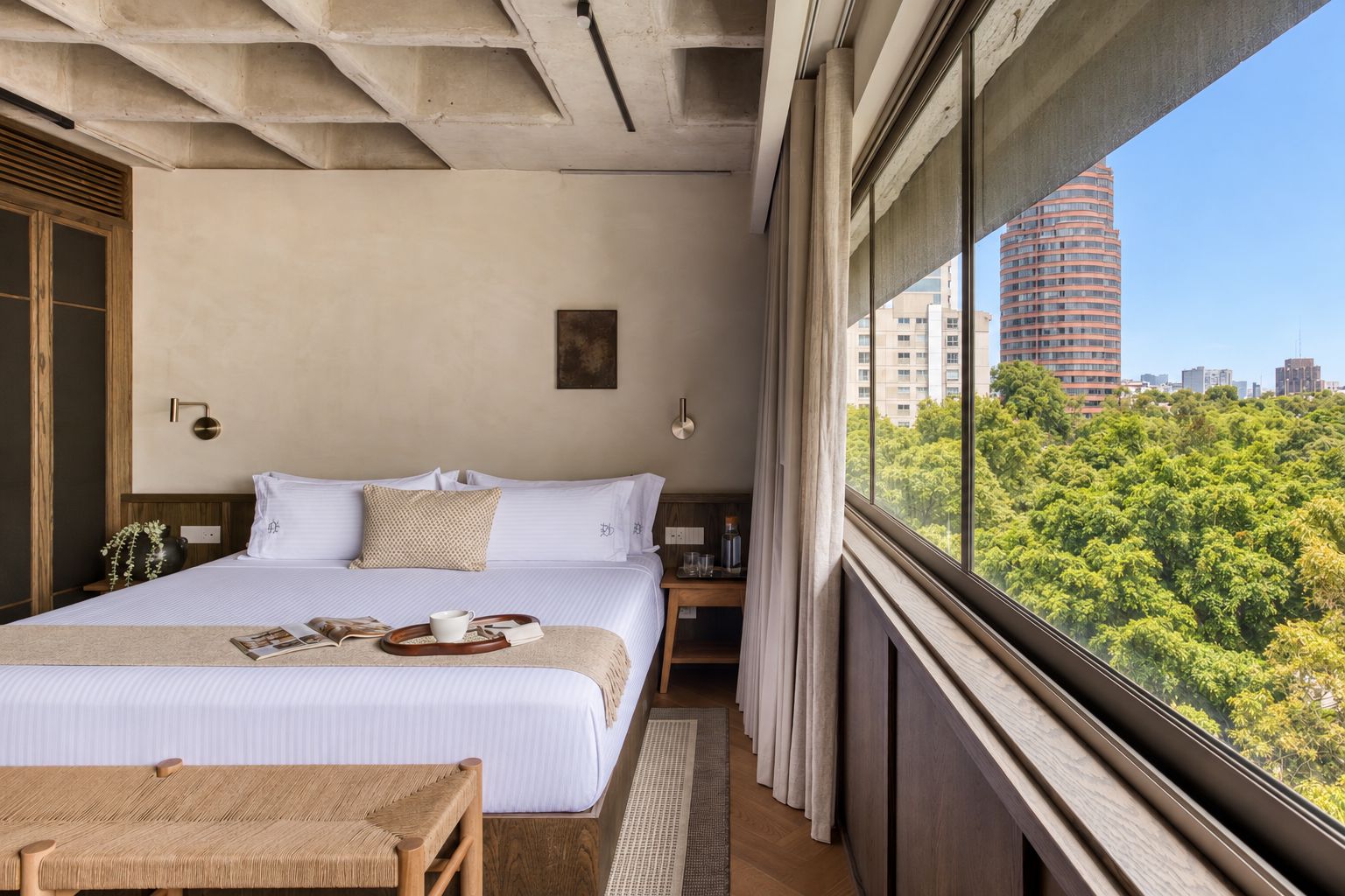 A bedroom with a large bed, a bedside table, a window with a view of a cityscape and trees.