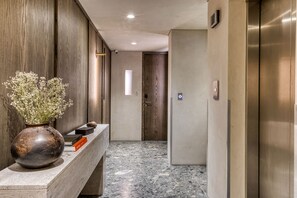 A hallway with a marble floor, a wooden wall, a vase with flowers, and a door with a number. - Collections by ULIV Darío (Ciudad de México)