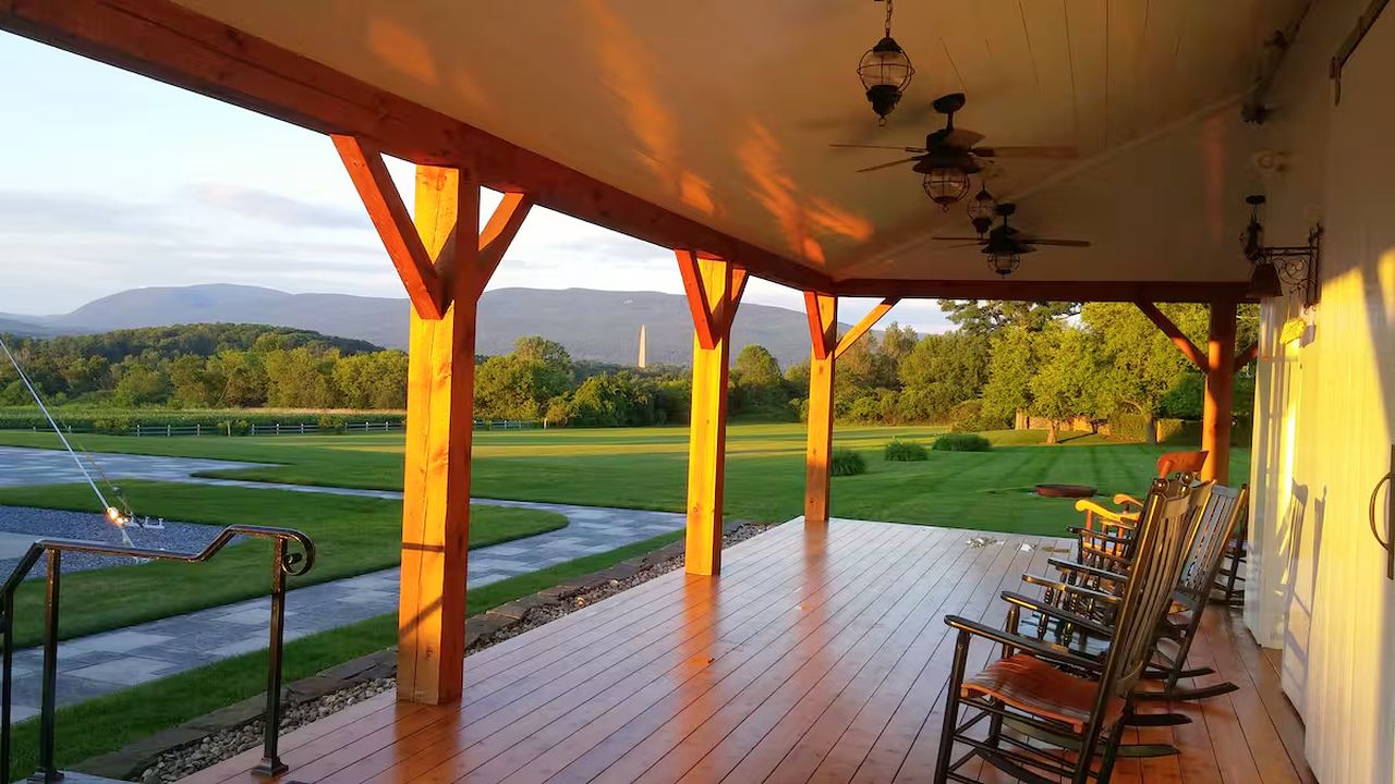 Eine überdachte Veranda mit Holzbalken, einem Pool und Stühlen.