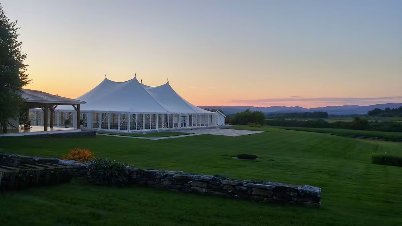 A large white tent structure with a covered patio area, surrounded by a well-maintained lawn and stone wall.