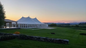 A large white tent structure with a covered patio area, surrounded by a well-maintained lawn and stone wall.