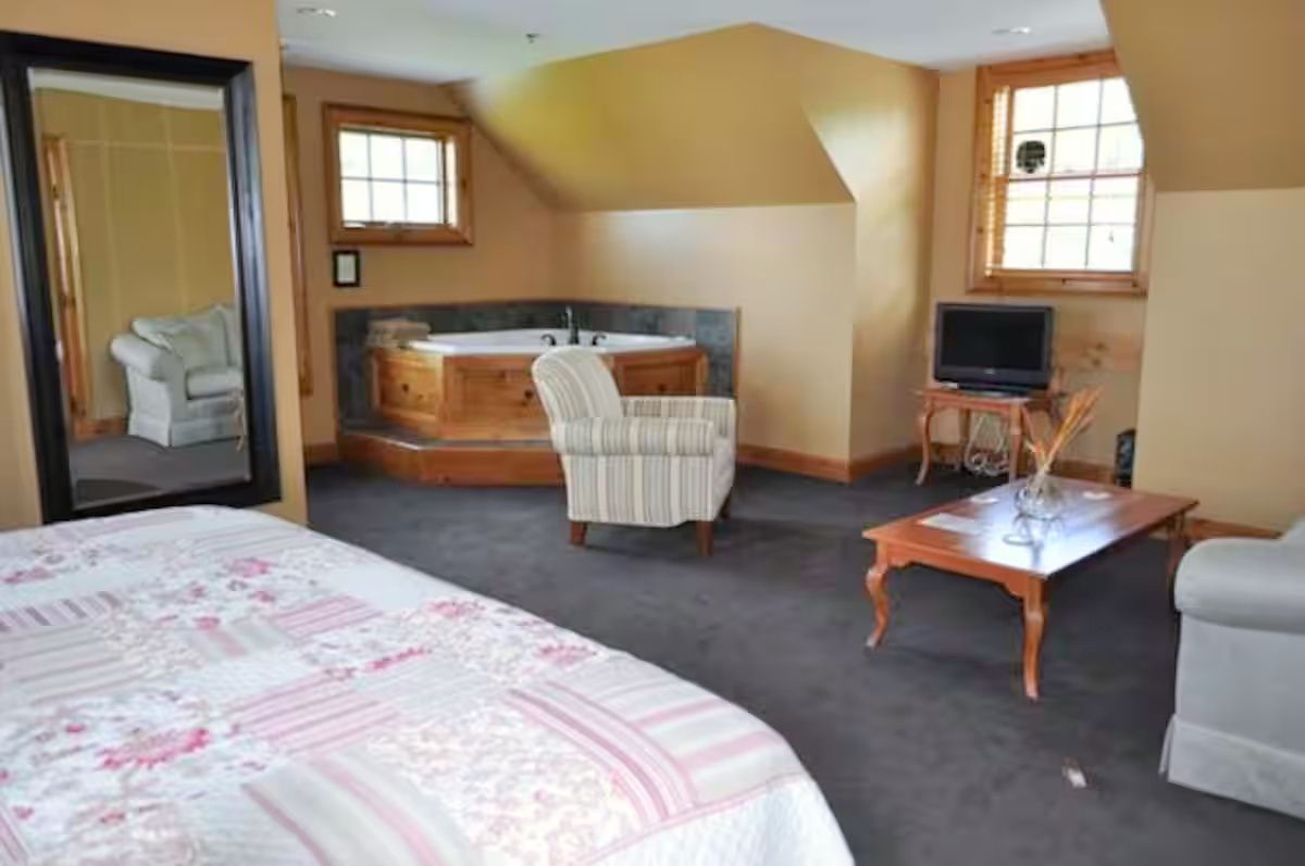 A bedroom with a large bed, a sitting area with a chair, a small table, a television, and a window.