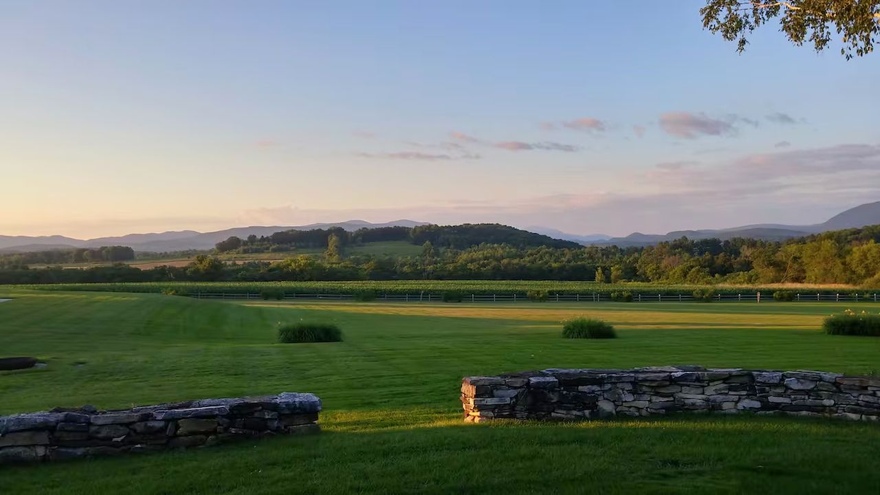 A rural landscape with a stone wall, grassy fields, and distant hills.