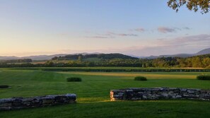 A rural landscape with a stone wall, grassy fields, and distant hills.