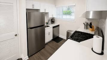 A modern kitchen with white cabinets, a stainless steel refrigerator, a gas stove, and a window with blinds.