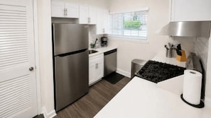 A modern kitchen with white cabinets, a stainless steel refrigerator, a gas stove, and a window with blinds.