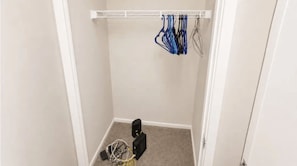 A small closet with a white door, a white ceiling, and a white wall. There is a white shelf with a white object on it.