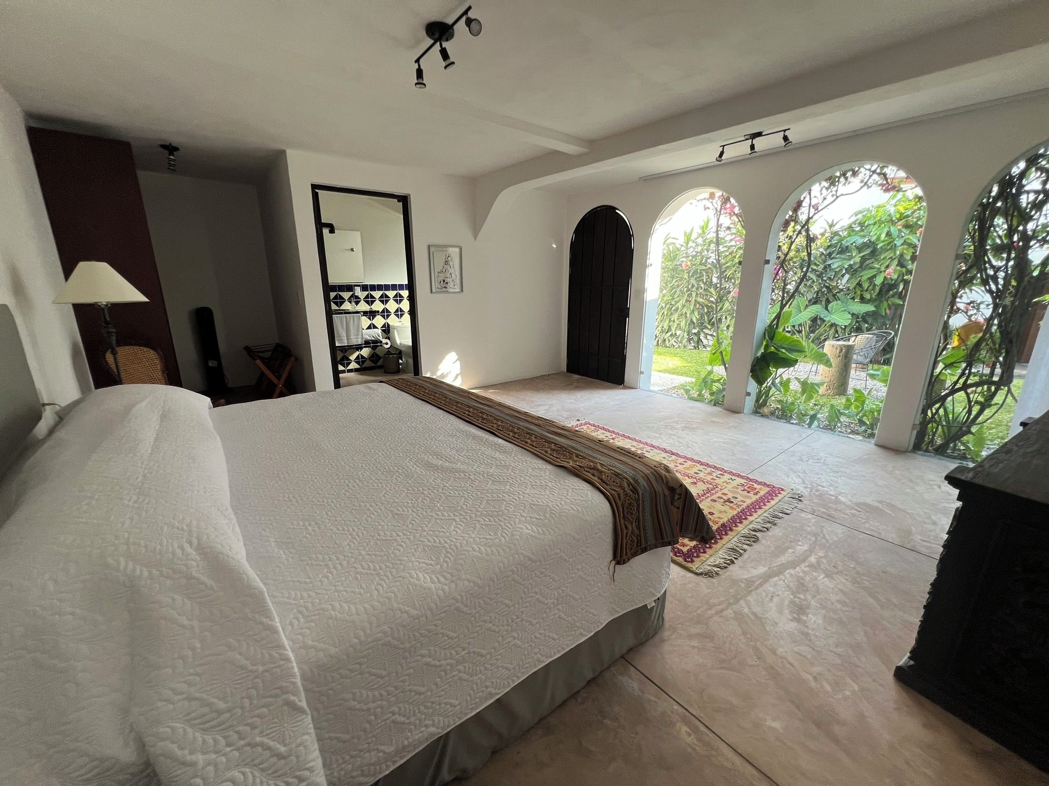 Une chambre avec un grand lit, une salle de bain et une vue sur un jardin, visible à travers une fenêtre en arc de cercle.