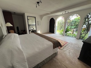 A bedroom with a large bed, a bathroom, and a view of a garden through an arched window.