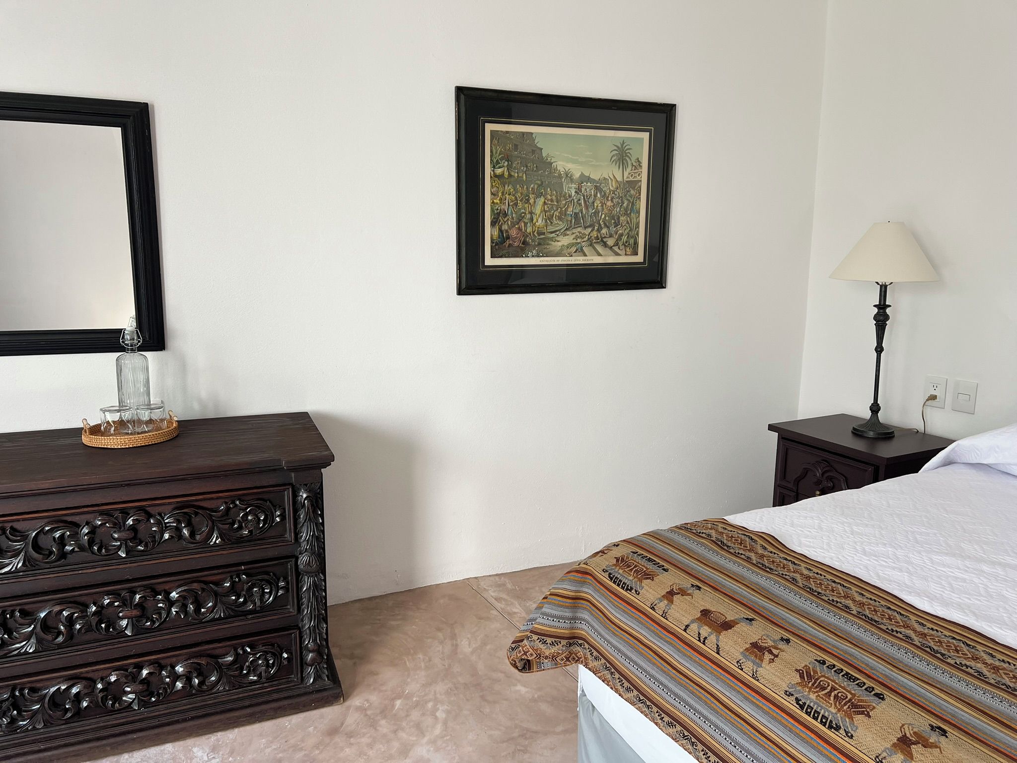 Une chambre à coucher avec un lit, une commode, une lampe et un tableau encadré au mur.