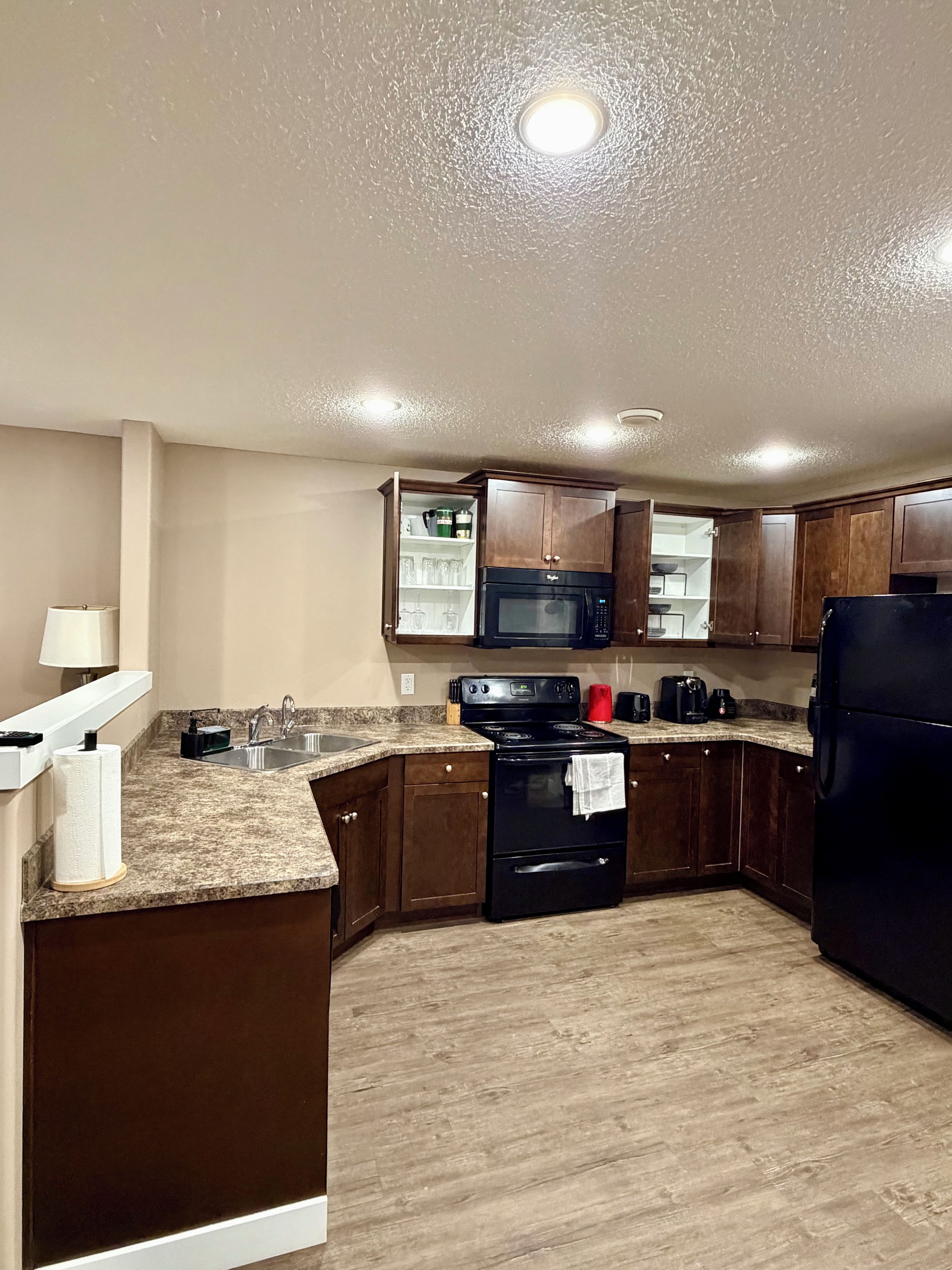 A kitchen with a granite countertop, stainless steel sink, black stove, and wooden cabinets.