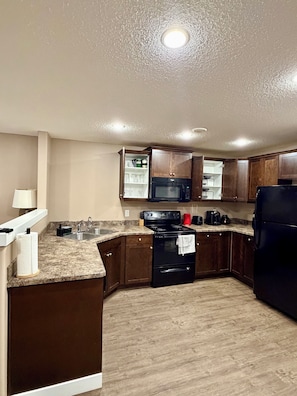 A kitchen with a granite countertop, stainless steel sink, black stove, and wooden cabinets. - Modern & Cozy 2BR | Near Refinery, Airport & Central Regina (Regina)