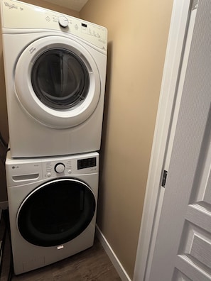 A stacked washer and dryer unit in a room with a wooden floor and a white door. - Modern & Cozy 2BR | Near Refinery, Airport & Central Regina (Regina)