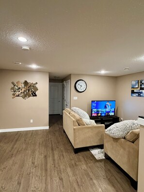 A living room with two sofas, a television, a clock, and a decorative wall piece. - Modern & Cozy 2BR | Near Refinery, Airport & Central Regina (Regina)