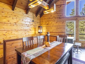 A wooden interior with a long dining table, chairs, and a hanging light fixture. - Cozy Big Bear Cabin • Sleeps 10 • Pet Friendly! (Big Bear)