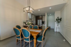 A modern dining area with a wooden table and chairs, a chandelier, and a kitchen in the background. - 2 - bedroom skyline Oasis Over Santo Domingo DR (Santo Domingo)