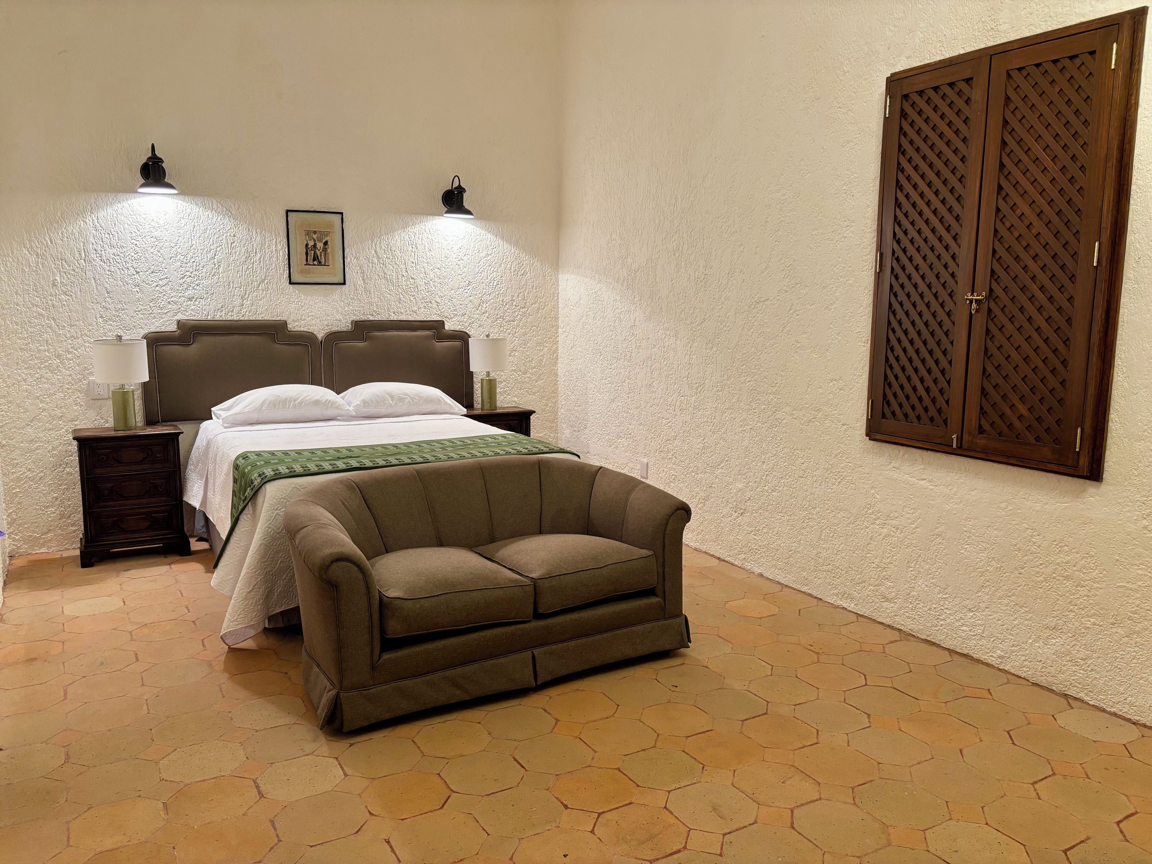 A bedroom with a bed, two bedside lamps, a nightstand, a sofa, and a large wooden door.