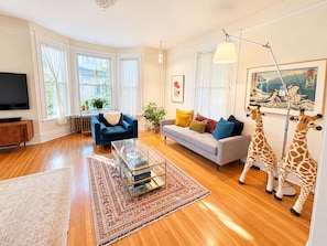 A living room with a sofa, armchairs, a coffee table, a TV, and two giraffe statues. - Historic 4BR and 3 Bath, University District Home, Sleeps 8, Near UM & Downtown (Missoula)