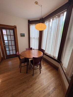 A dining area with a wooden table and chairs, a hanging light fixture, and a window with curtains. - Historic 4BR and 3 Bath, University District Home, Sleeps 8, Near UM & Downtown (Missoula)