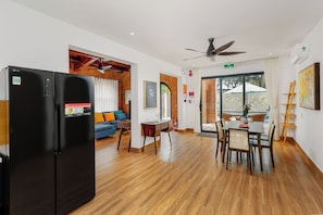 A modern kitchen with a black refrigerator, a dining area with wooden furniture, and a living room with a blue sofa. - Salt Villa 5BR Beachfront An Bang Beach Hoi An by Beachside Boutique Homes (Đà Nẵng)