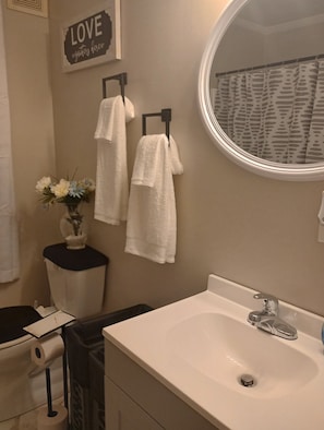 Un bagno con lavandino, specchio, porta asciugamani e un cartello appeso al muro.