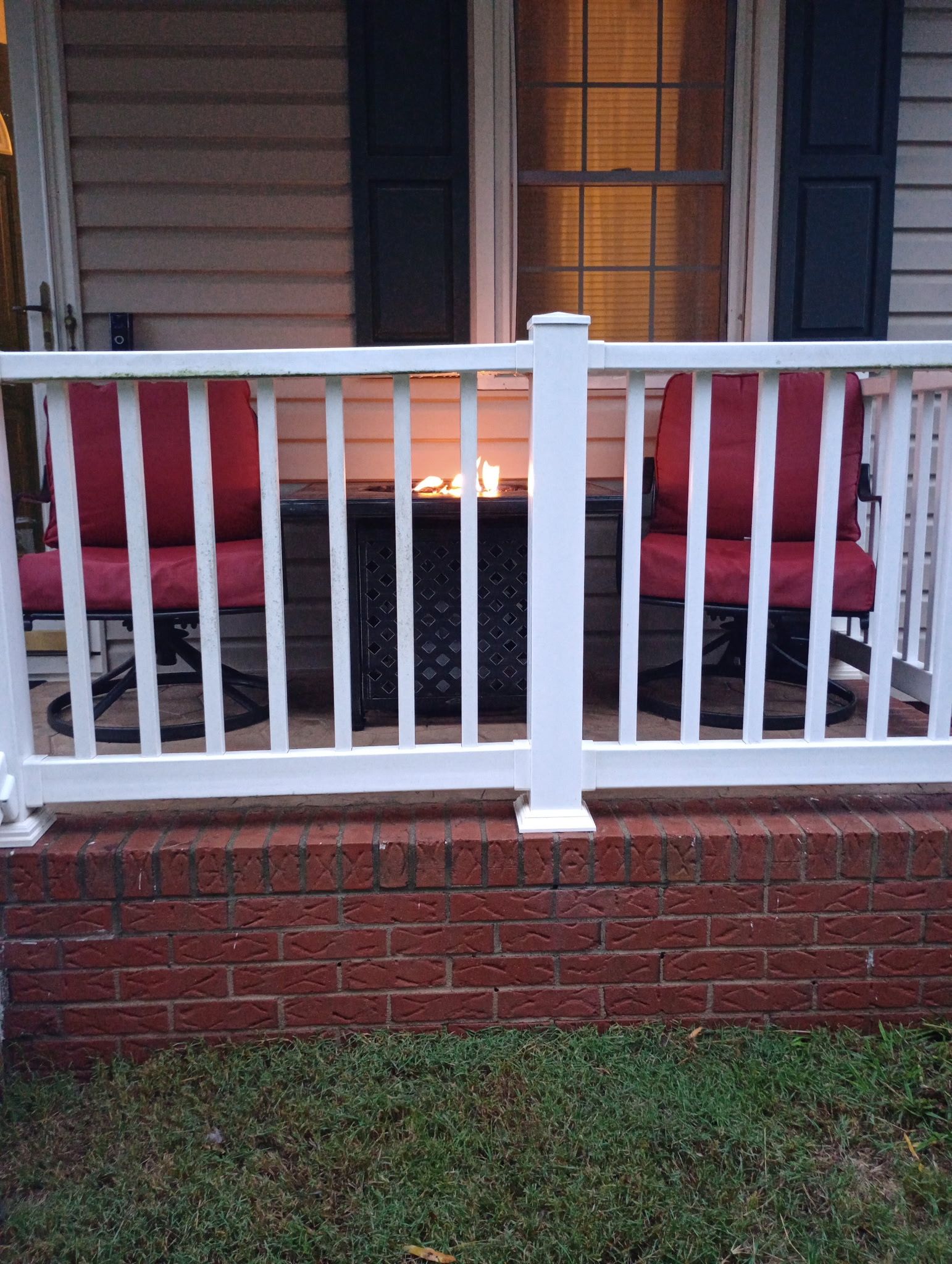 A brick porch with a white railing, two red chairs, and a fire pit.
