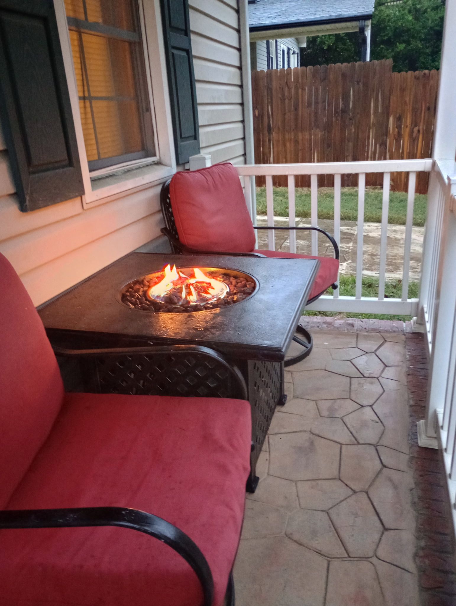 Eine Terrasse mit Tisch und Stühlen, einer Feuerstelle und einem Holzzaun im Hintergrund.