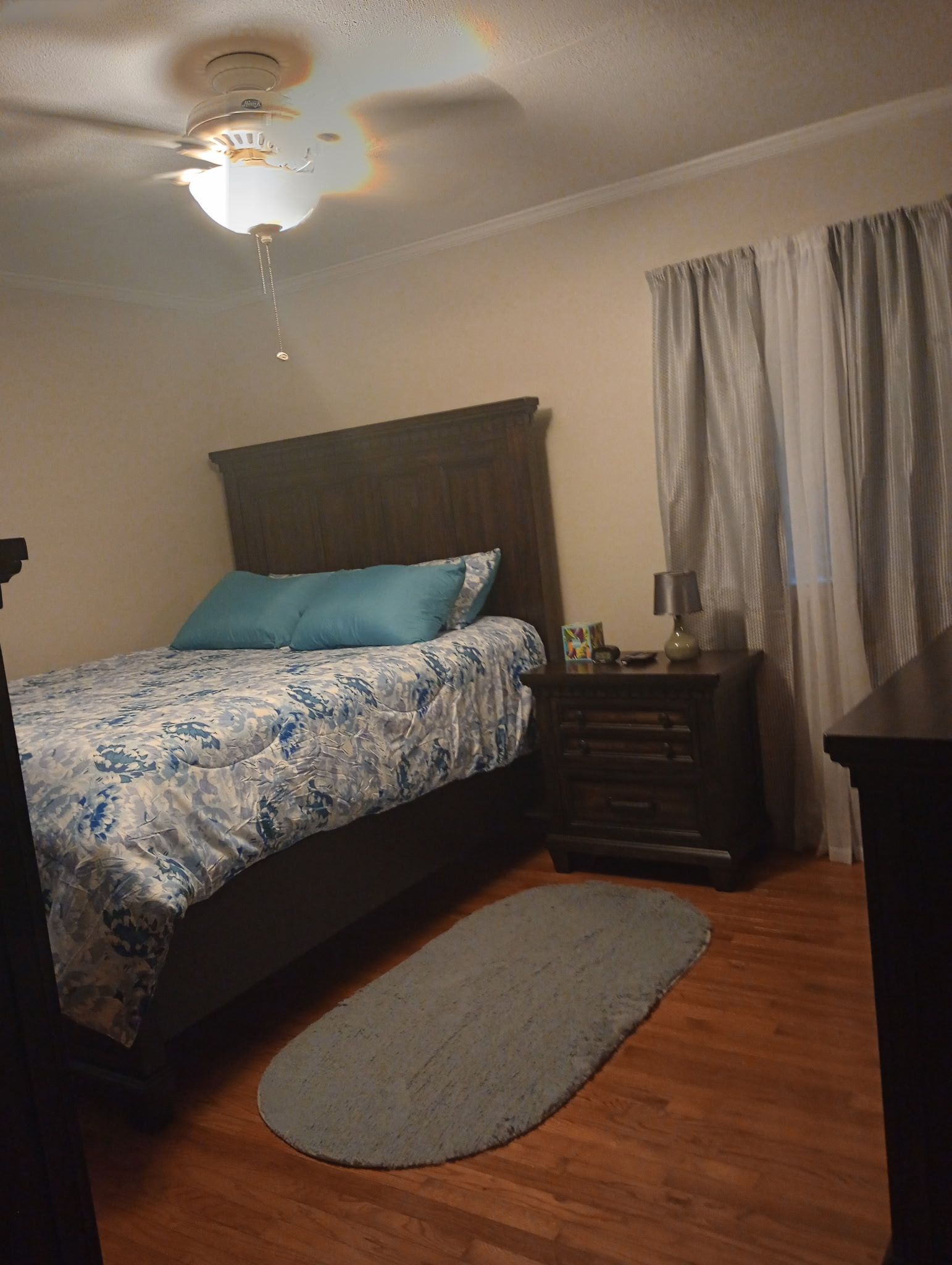 A bedroom with a bed, a nightstand, a lamp, a rug, and a ceiling fan.