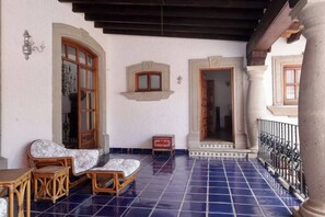 A covered patio with a tiled floor, a wooden bench, a small table, and a decorative wall-mounted light fixture. - Up to 15 bedroom house in Cuernavaca perfect for large groups (Cuernavaca)