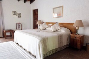 A bedroom with a large bed, two bedside tables with lamps, a wooden chair, and a small table. - Up to 15 bedroom house in Cuernavaca perfect for large groups (Cuernavaca)