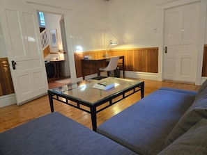 Una habitación con una mesa de centro de vidrio, un sofá azul, un escritorio de madera y una silla.