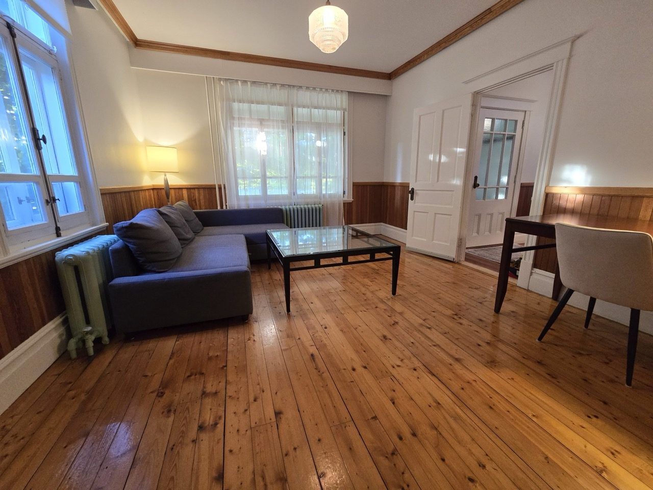Ein Zimmer mit Holzboden, einem Sofa, einem Glastisch, einem Sessel und einer Heizung.