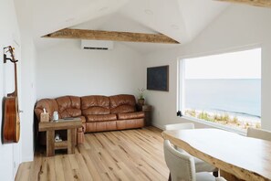 Une pièce avec un plafond en bois, un canapé en cuir marron, une table en bois et une vue sur la mer par une grande fenêtre.