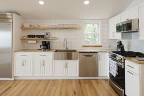 Une cuisine moderne avec des meubles blancs, des appareils en acier inoxydable et un plancher en bois.