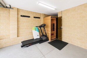 A room with a treadmill, a wooden cabinet, and a door leading to another room. - The Duchess on Duke | Mineral Spa & Sauna | 3BR, Sleeps 6 | Beach 5 min (WA)