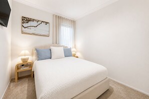 A bedroom with a bed, bedside tables, a lamp, a painting, and a window with curtains. - The Duchess on Duke | Mineral Spa & Sauna | 3BR, Sleeps 6 | Beach 5 min (WA)