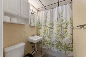 Een compacte badkamer met toilet, wastafel en douchegordijn met een bamboepatroon.