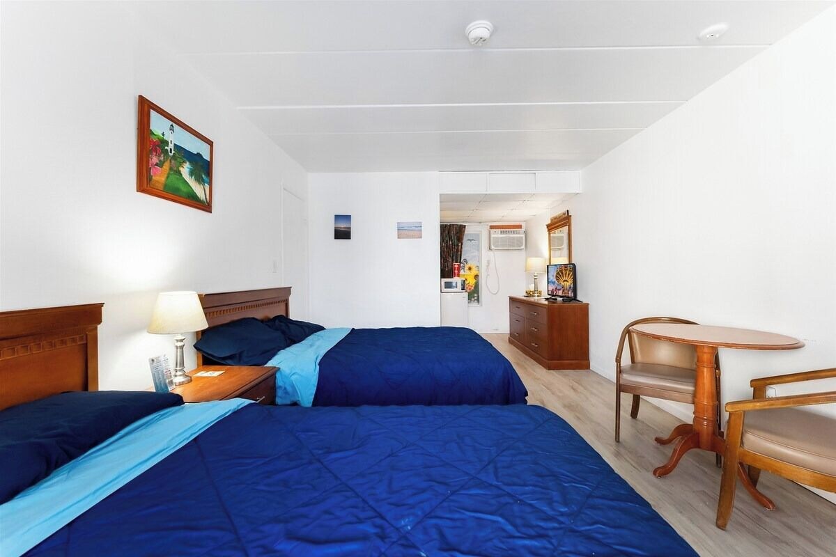 A hotel room with two beds, a wooden headboard, a small table, and a chair.