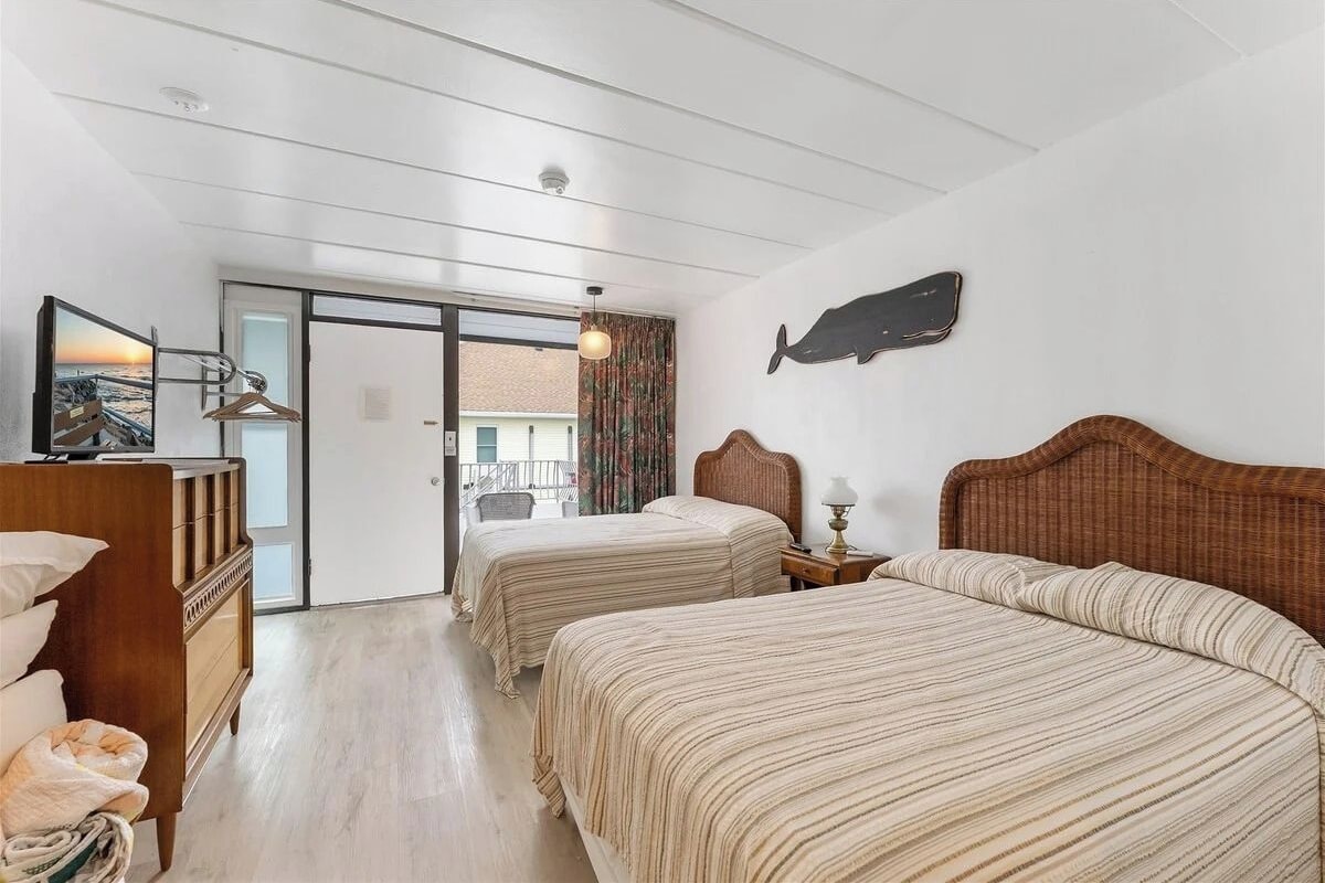 A hotel room with two beds, a wooden dresser, a television, and a view through a glass door.