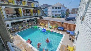 A swimming pool with lounge chairs and inflatable toys, surrounded by buildings. - The Sunflower Beach Club by Experience Vacation Rentals (Wildwood)