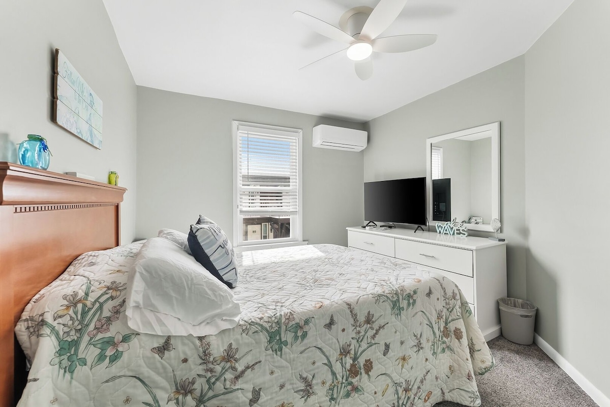 A bedroom with a bed, a dresser, a television, a ceiling fan, and a window.