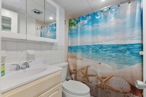 A bathroom with a sea-themed shower curtain, a white sink, a mirror, and a toilet. - The Madrid by Experience Vacation Rentals (Wildwood Crest)