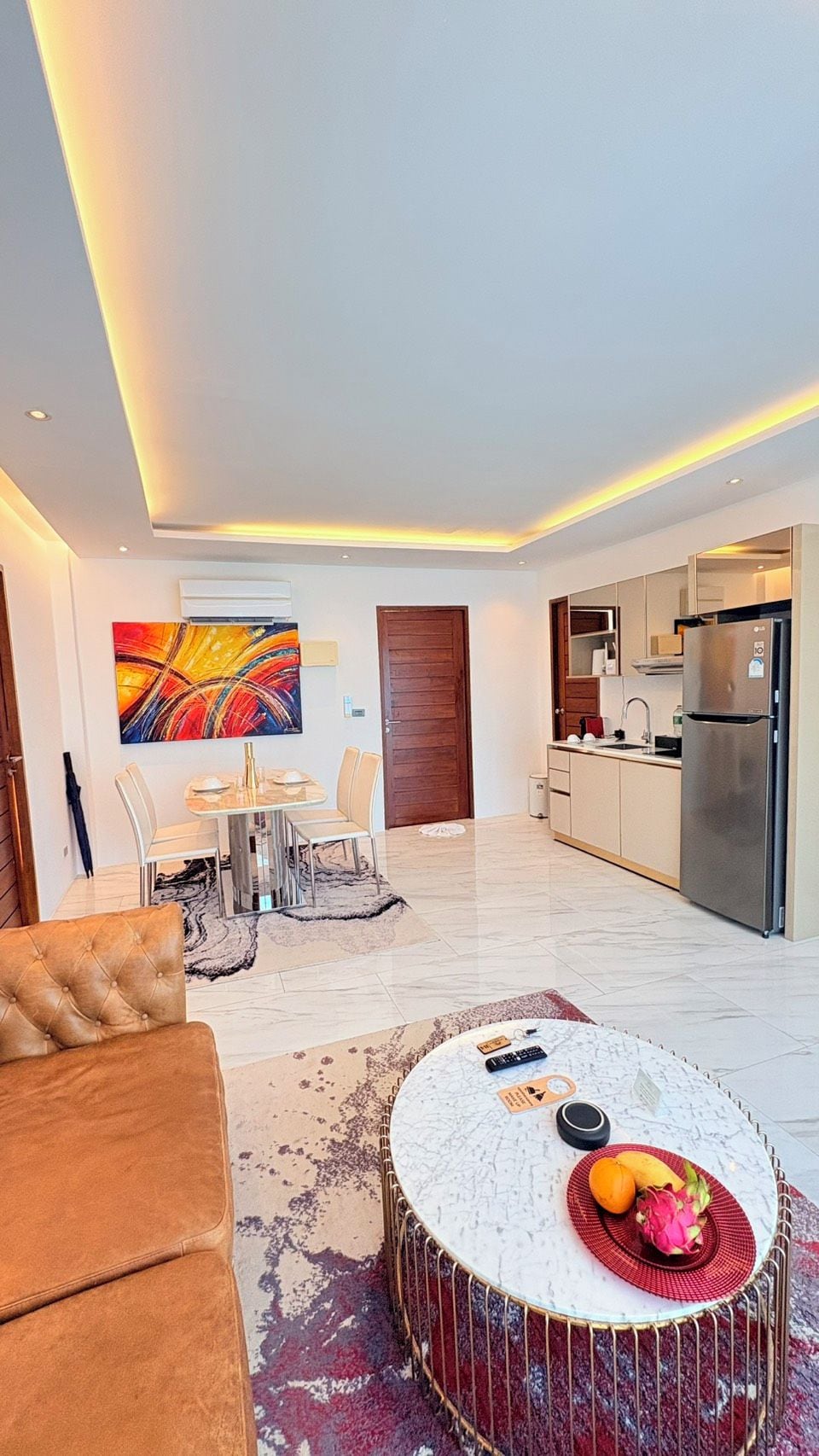 A modern living room with a dining area, a kitchen, and a red drum table with fruits.