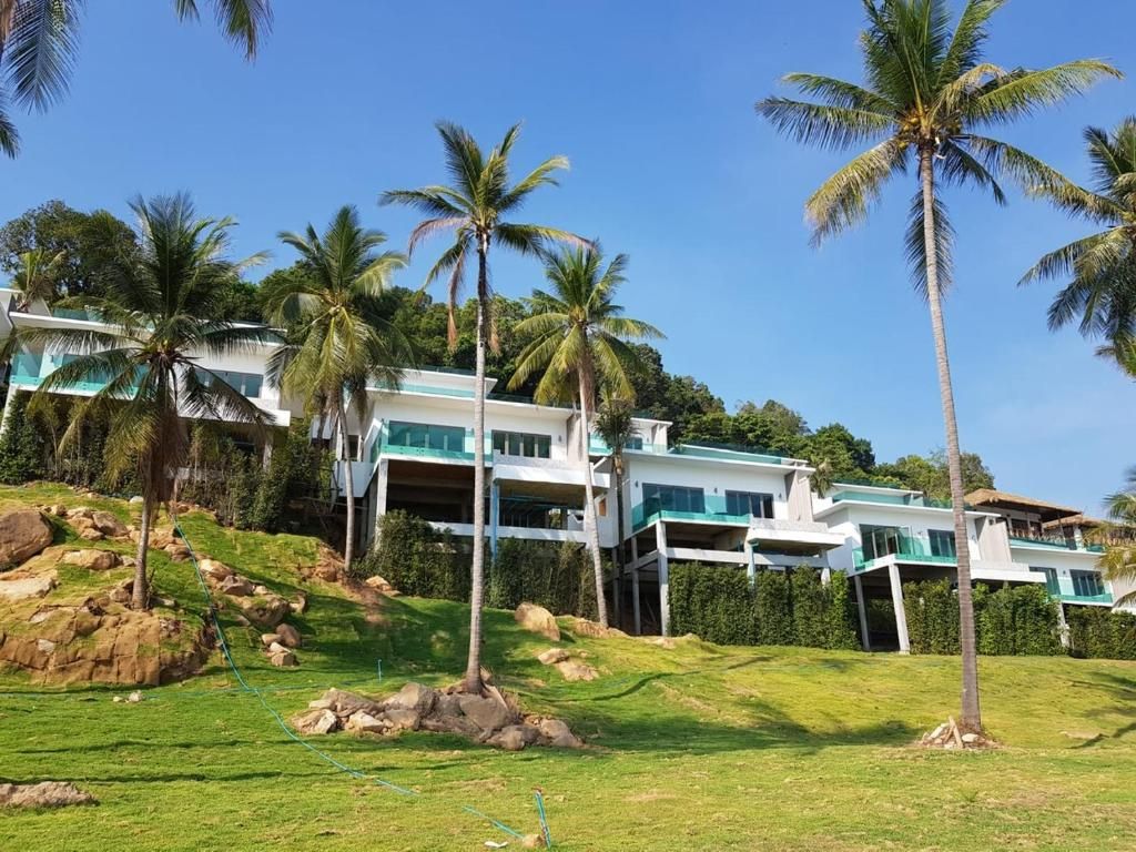 A multi-story building with a modern design, surrounded by palm trees and a grassy area.
